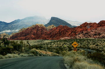 This photo shows the landscape of Red Rock Canyon National Conservation Area with layers of colourful red rocks, sandstone, and plants growing sparsely in the desert terrain.