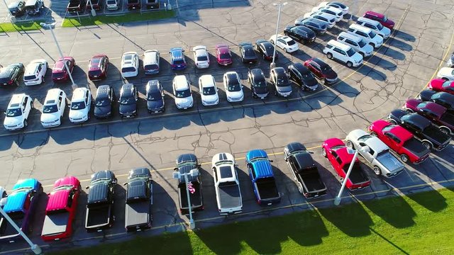 Looking straight down on new car lot, many vehicles for sale, glistening in the sun, aerial view.