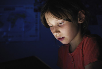 Dolly shot caucasian girl lying in bed playing tablet in social internet in dark blue light under blacket. Childhood, communication and technology concept