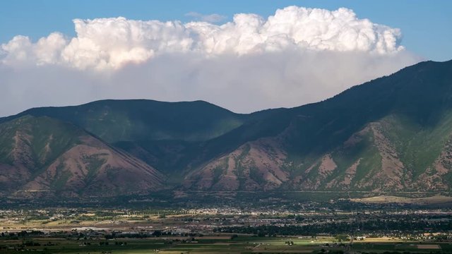 Time lapse of smoke from wild fire burning over mountains viewed from a long distance away across Utah Valley.