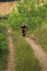 Fototapeta premium The dirt road goes into the distance, through the trees to the sandy slope of the mountain, along it comes a young woman.