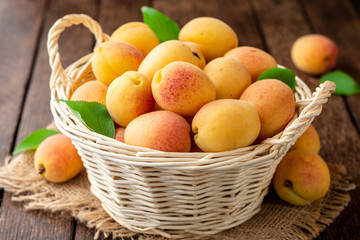 Fototapeta na wymiar Fresh apricots in wicker basket on dark wooden background
