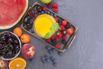 Different berries and fruits on a gray background, fresh fruit juice. Vitamins and detox food. Copy space.