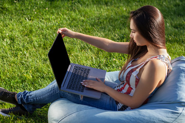 Young cute girl with laptop, sit on bean bag in garden or park, on green grass. Online shopping concept