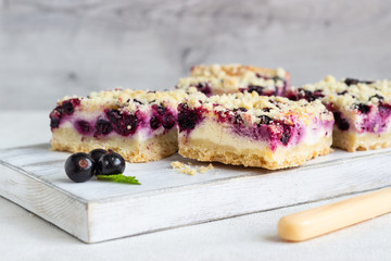 Black currant cake. Cheesecake bars with lemon, black currant and streusel on a white wooden cutting board.