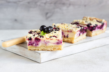 Black currant cake. Cheesecake bars with lemon, black currant and streusel on a white wooden cutting board.
