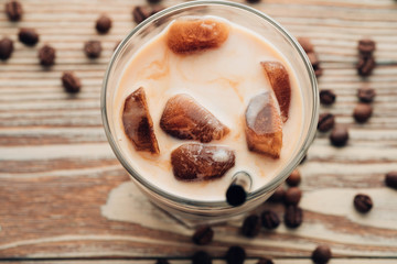 Cold coffee glass with ice cubes on wooden table background. Ice coffee. Copy space.