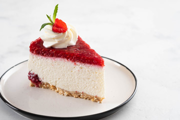 Cheesecake slice with fresh raspberries and mint leaves on a white plate. Copy space.