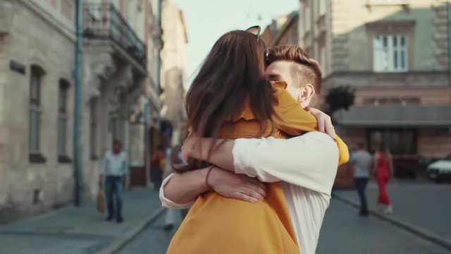 Handsome young man in trendy wear waits for his girlfriend lifts her up in a hug at the city center. Romantic date, real emotions, true love. Couple goals, happiness, love story