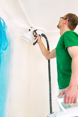Man painting walls using spray gun.