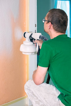 Man painting an interior wall using a spray gun.