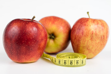 Red apples and a measure of tailor on a white table. Ripe fruits and a tailor's centimeter.