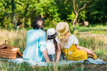 back view of parents and daughter sitting on blanket at picnic