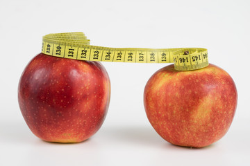 Red apples and a measure of tailor on a white table. Ripe fruits and a tailor's centimeter.