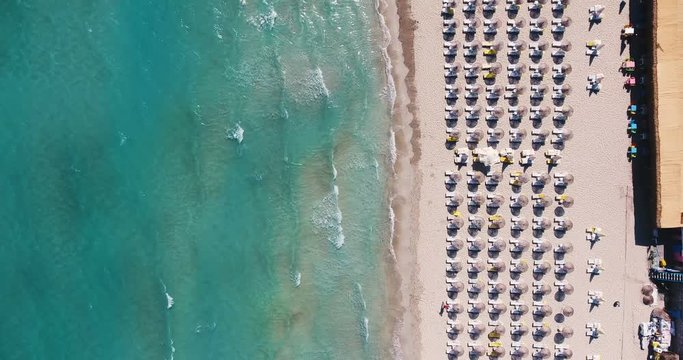 Aerial - Umbrellas on the beach. Top down view of waves hitting sandy shore