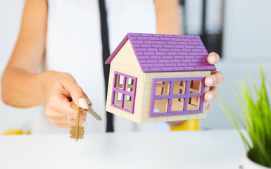 Young businesswoman or real estate agent with hose model and keys in hands closeup.
