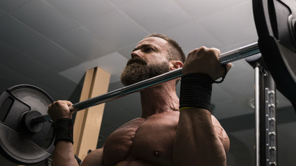Hombre fuerte con grandes músculos levantando peso mientras entrena en el gimnasio. Ponerse en...