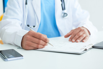 Closeup of male doctor's hands taking notes or fills in the client's medical card or prescribes medication. Ward round, patient visit check, medical calculation and statistics concept.