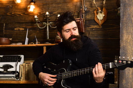 Man bearded musician enjoy evening rehearsing performance at home, wooden background. Boost your skills. Guy in cozy warm atmosphere learn new song chords. Man with beard holds black electric guitar