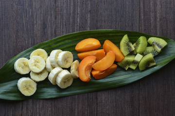 Chopped fruits (kiwi, apricot, banana) on green leaf. Top view