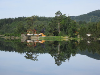 Fototapeta na wymiar SunReflection of house and trees in crystal clear lake water