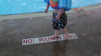 No running sign on the floor at the pool with kids feet going by.