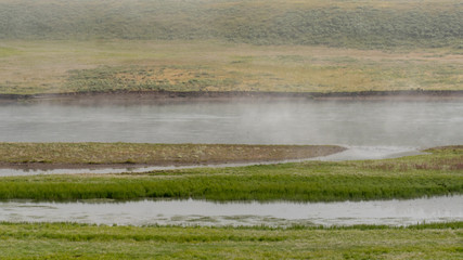 Steam rising off river with grass and fields