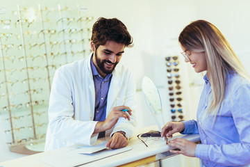 Fototapeta premium Woman choosing her new glasses at optics store with help of ophthalmologist