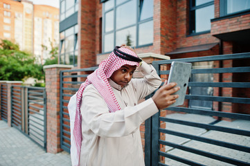 Middle Eastern arab man posed on street against modern building with tablet at hands.