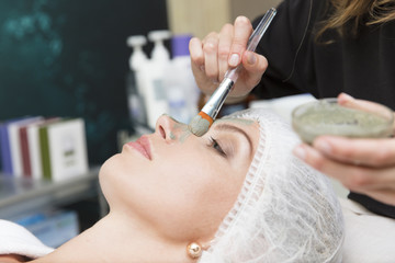 Young beautiful girl receiving facial mask in spa beauty salon from cosmetologist