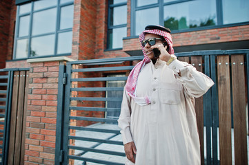 Middle Eastern arab business man posed on street against modern building with sunglasses, speaking on mobile phone.