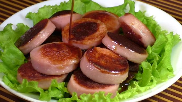Stream of soy sauce is poured onto a dish of fried sausages and lettuce close up