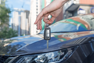 Car key in hand on car background