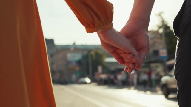Young romantic couple holds their hands in the city center on a bright sunlight. Happiness, romantic atmosphere, dating. Togetherness, romance. Love story