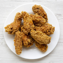 Chicken wings on a round white plate over white wooden surface, view from above. Top view, flat lay.