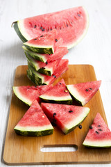 Many slices of juicy watermelon on bamboo board over white wooden background. Side view, close-up.