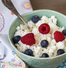 Cottage cheese in blue bowl with raspberries and blueberries on a napkin. Healthy Breakfast.