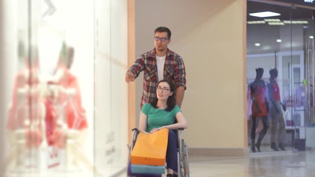 Guy rolls a disabled girl in a wheelchair at the Mall. They made purchases.
