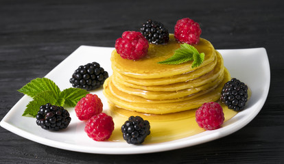 pancakes with honey and blackberries and raspberries on a white plate