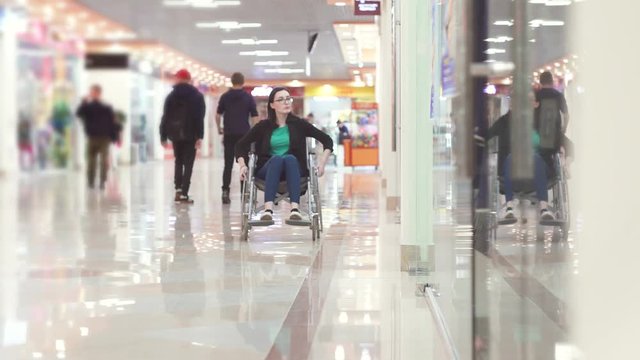 Woman with a disability in a wheelchair rides to the shopping center and looks at the windows