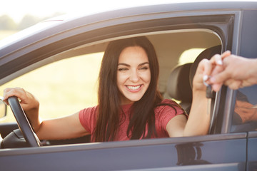 Happy Cuacasian young female takes car key from her husband, recieves expensive gift, going to drive automobile, has broad smile, being in high spirit. People, transport and driving concept.