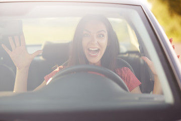 Emotions, driving and speed concept. Surprised female driver gestures with both hands, likes risk, takes off hands from wheel while drives car, has glad and shocked expression, enjoys speed on road
