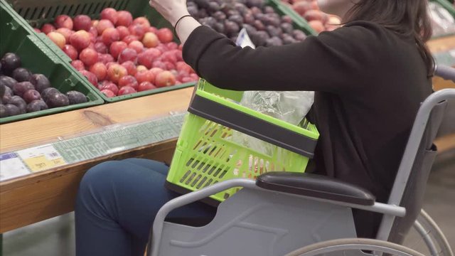 A woman with a disability in a wheelchair shopping in the supermarket chooses fruits and puts them in a package.Close up
