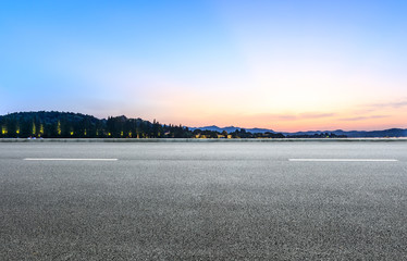 Empty asphalt road and hills silhouette at sunset
