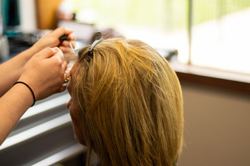 Fototapeta premium Blonde woman receiving haircut at a salon. Woman with blonde highlights. Hair foils on a female client. Master stylist cutting hair