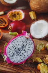 Raw fresh exotic fruits on wooden board and dark background. Healthy lifestyle, organic food. Dragon fruit, passionfruit, tamarillo, coconut, physalis, selective focus