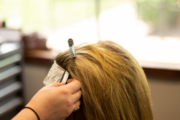 Fototapeta premium Blonde woman receiving haircut at a salon. Woman with blonde highlights. Hair foils on a female client. Master stylist cutting hair