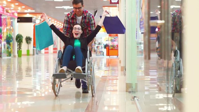 A man is lucky after shopping a disabled woman in a wheelchair at the Mall.They're having fun, they're laughing.Slow mo