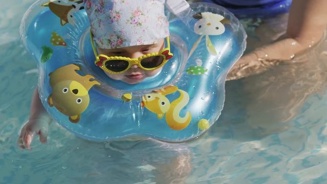 Cute baby swimming in the pool with an inflatable ring around his neck outdoors. The concept of a healthy lifestyle for children. Mom and baby are swimming