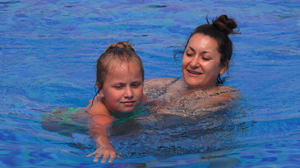 Pretty little girl and her mother swimming and playing together in the pool, close up